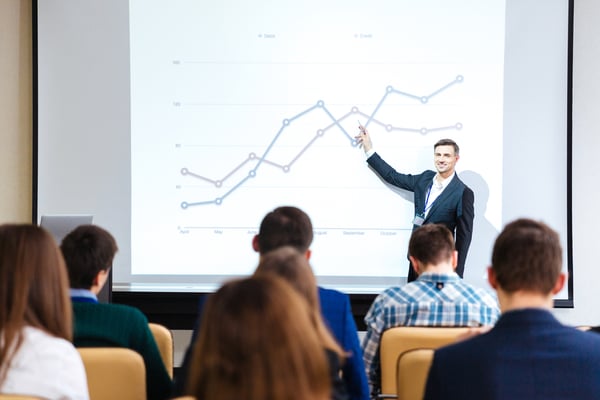 Smiling handsome speaker standing and explaining graphs on business conference in meeting hall